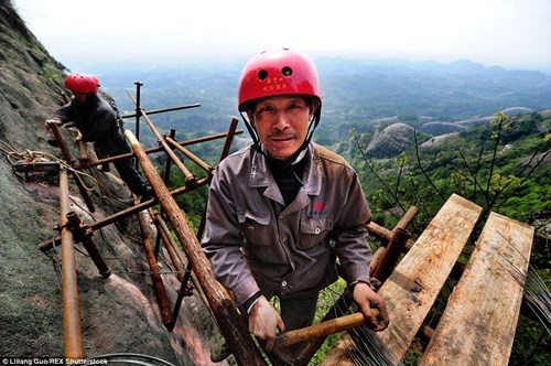 Một công nhân đang cố gắng gắn các thanh gỗ vào vách núi để mở đường