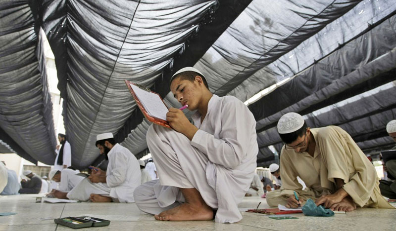 Học sinh Pakistan ngồi trên sàn làm bài thi tại Chủng viện Hồi giáo Jamia Binoria ở Karachi, Pakistan ngày 8/6/2013. Binoria là một trong những chủng viện mẫu, đã sửa đổi giáo trình giảng dạy của mình bằng việc bổ sung các môn học như máy vi tính, toán học và khoa học. Ảnh: AP