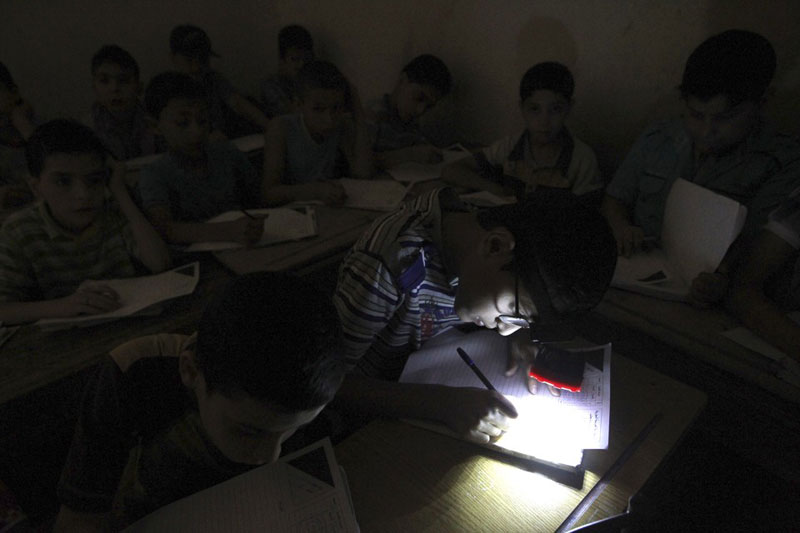 Học sinh đeo đèn trên đầu do thiếu điện khi tham gia kỳ thi cuối năm ở một trường thuộc al-Sha’ar , Aleppo, Syria ngày 5/6/2013. Ảnh: Reuters