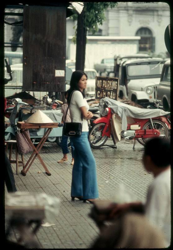 Quần ống loe là dấu ấn đặc trưng thời trang thập niên 70 cũng được các quý cô Sài Gòn đón nhận nhanh chóng. Phụ nữ Sài Gòn tại công trường Lam Sơn, Sài Gòn năm 1969, bên phải là cư xá Eden.